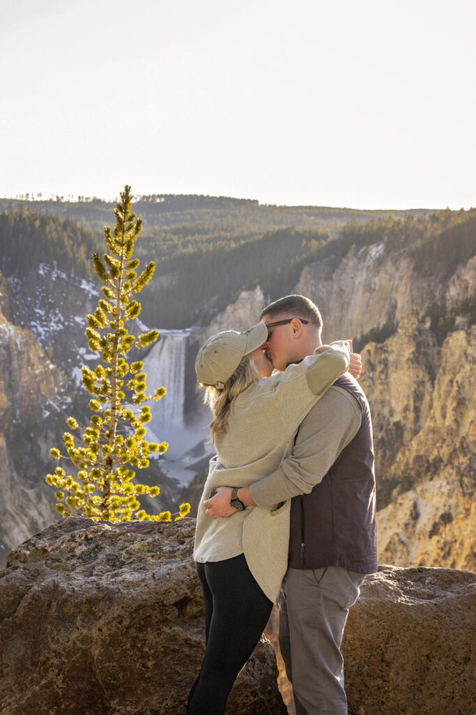 Couple standing at the overlook of Lower Falls in Yellowstone National Park at dusk.