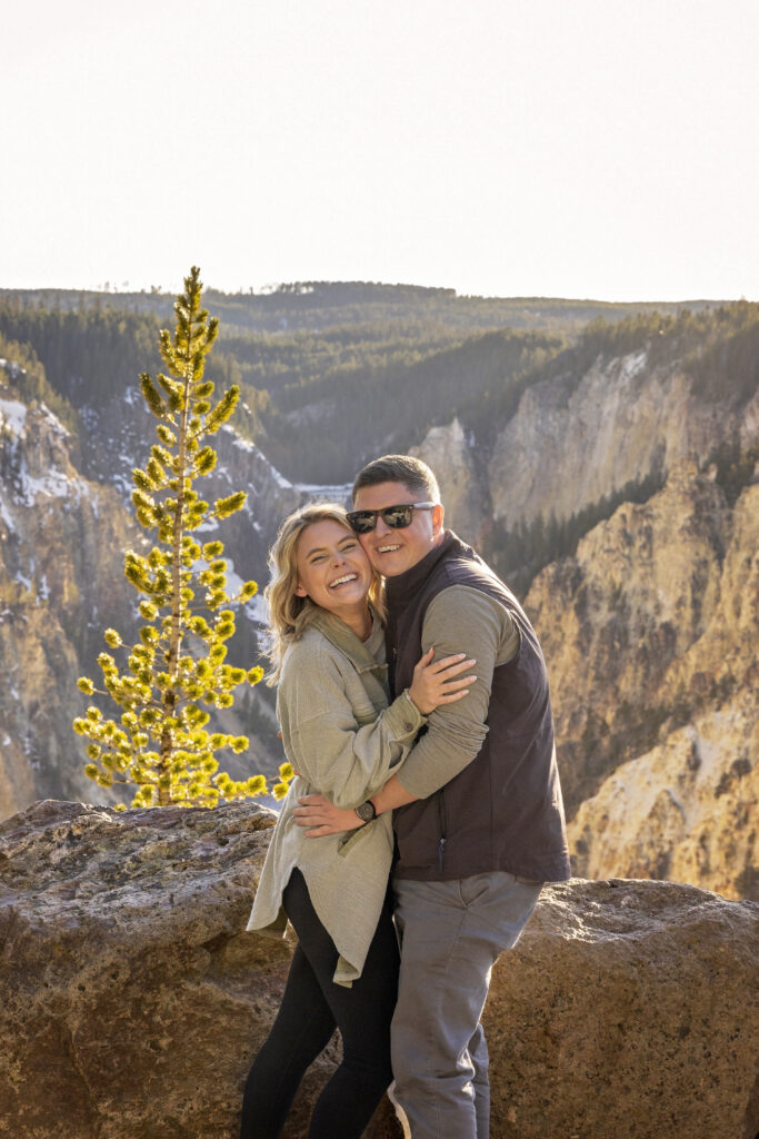 Couple posed side by side at sunset with waterfall and canyon in the background.