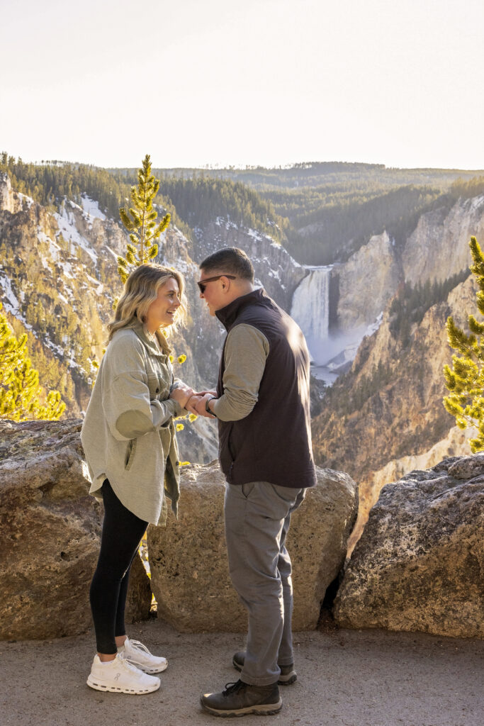Ashlyn and Kasey laughing and holding hands with a sweeping canyon vista behind them.