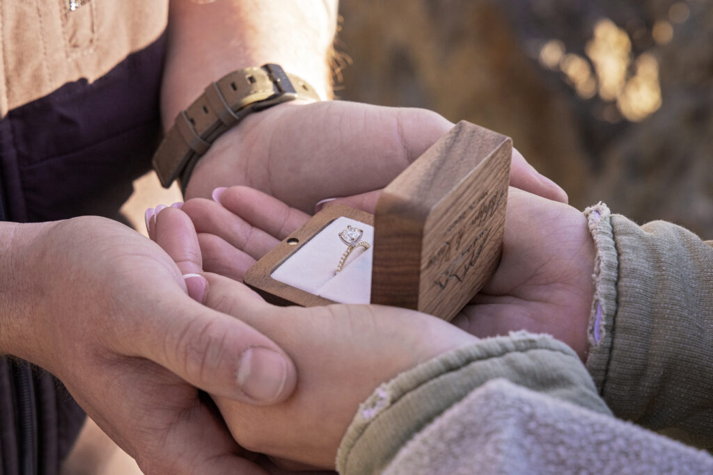 Close-up of sparkling engagement ring in open ring box in couple's hands in Yellowstone.