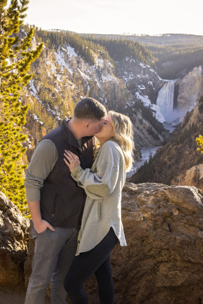Couple sharing a kiss with the iconic Yellowstone waterfall in the background.