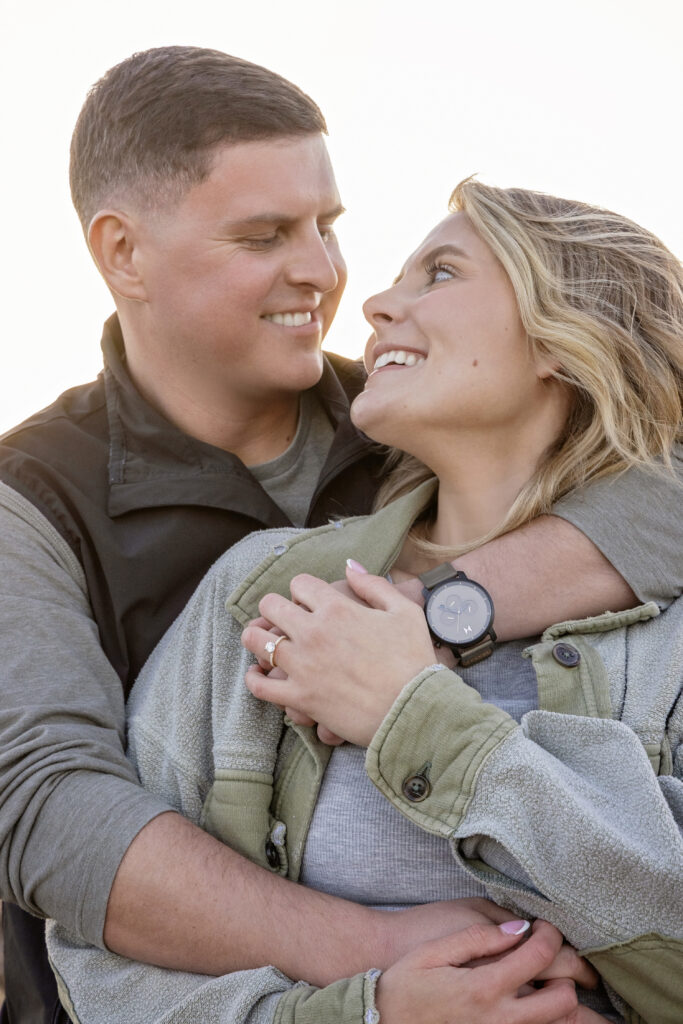 Artistic portrait of couple standing close together with soft golden light behind them.