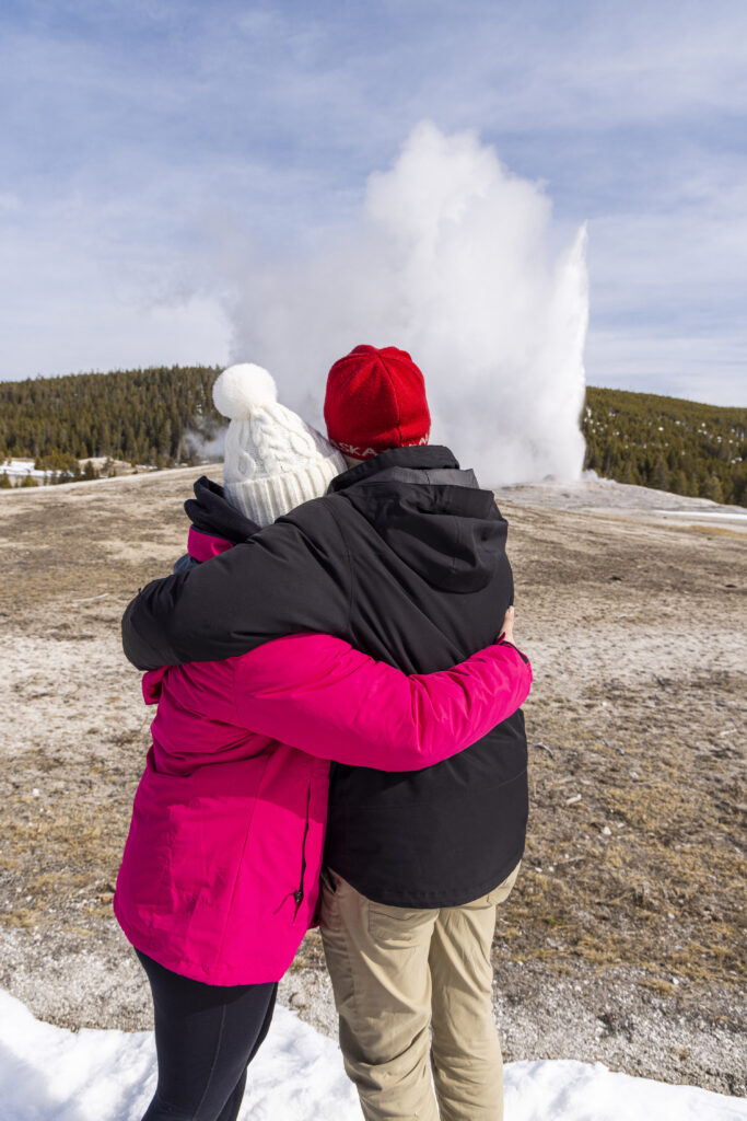 Newly engaged couple hugging while watching Old Faithful erupt in Yellowstone National Park.