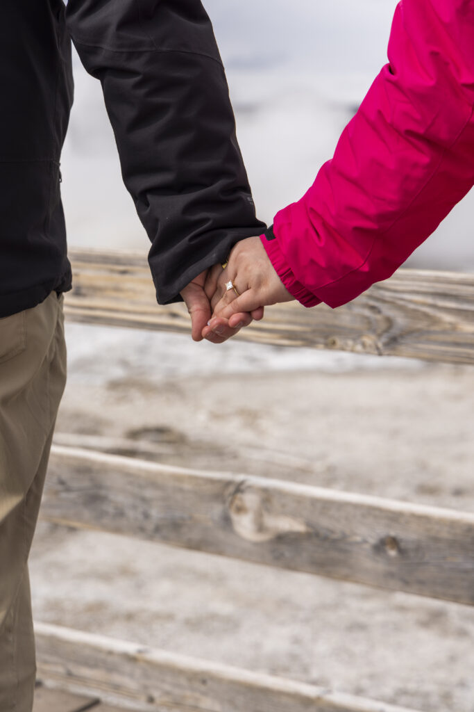 Close-up of newly engaged couple holding hands in the snow, showcasing Jill’s engagement ring.