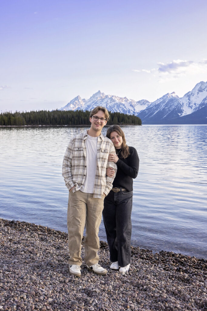 Avery and Riley take in the view from a lakeside rock, newly engaged and deeply connected.