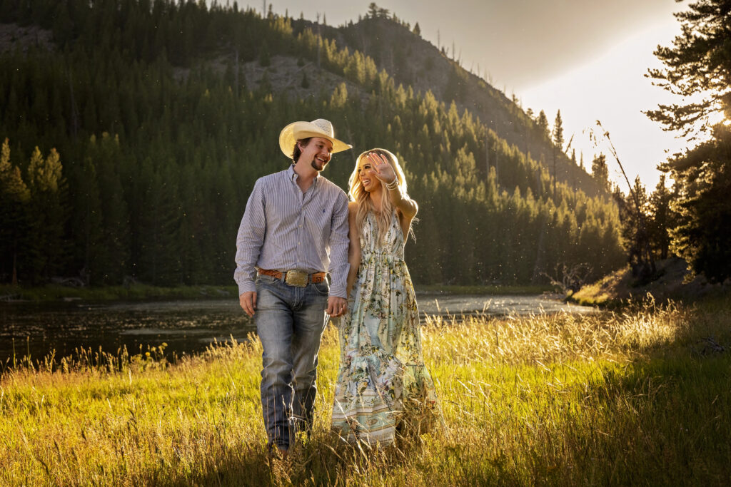 Couple walking along the Madison River at sunset, showing off engagement ring after Yellowstone surprise proposal